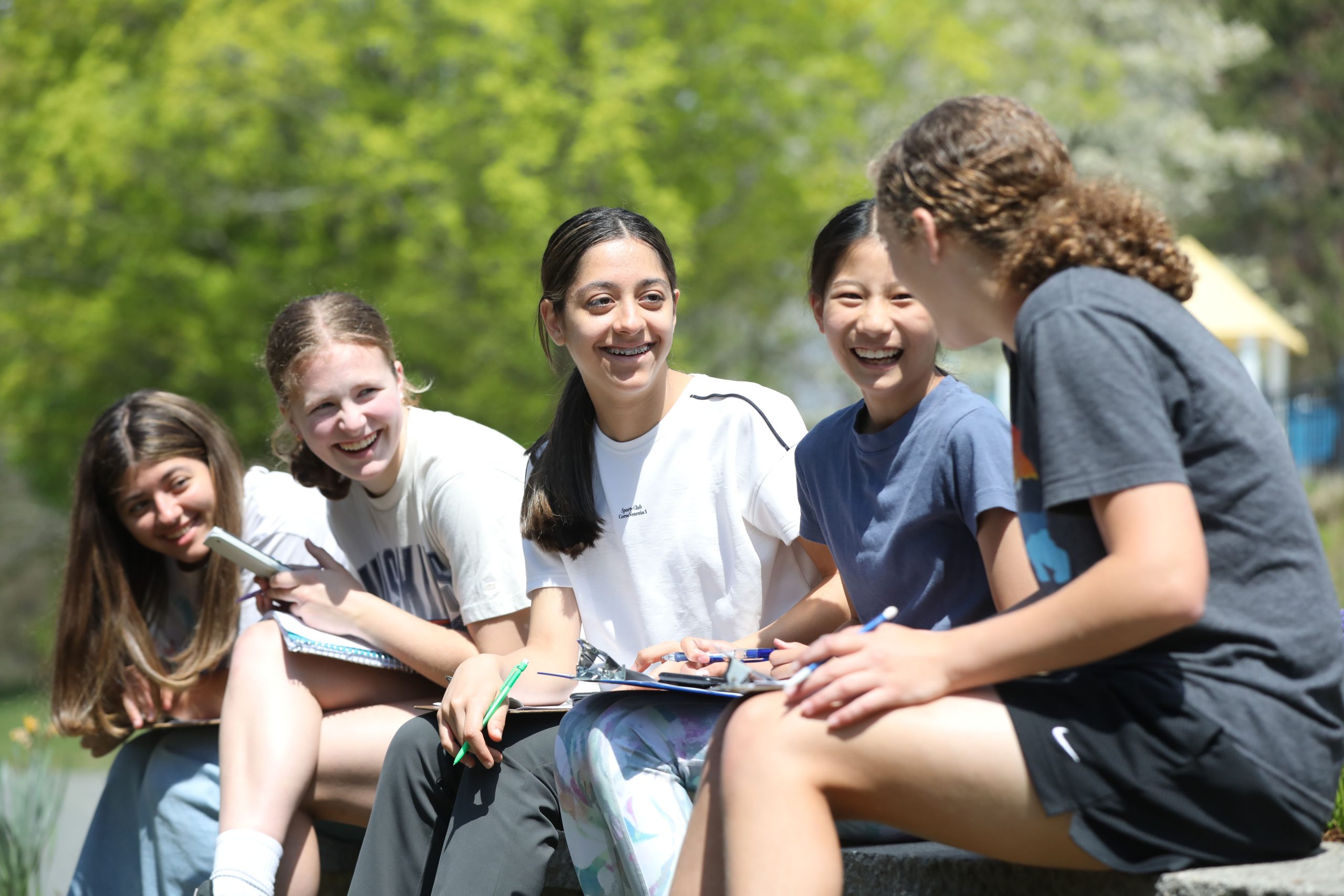 Bancroft School Worcester, MA students sitting on a wall outside laughing in the sun.